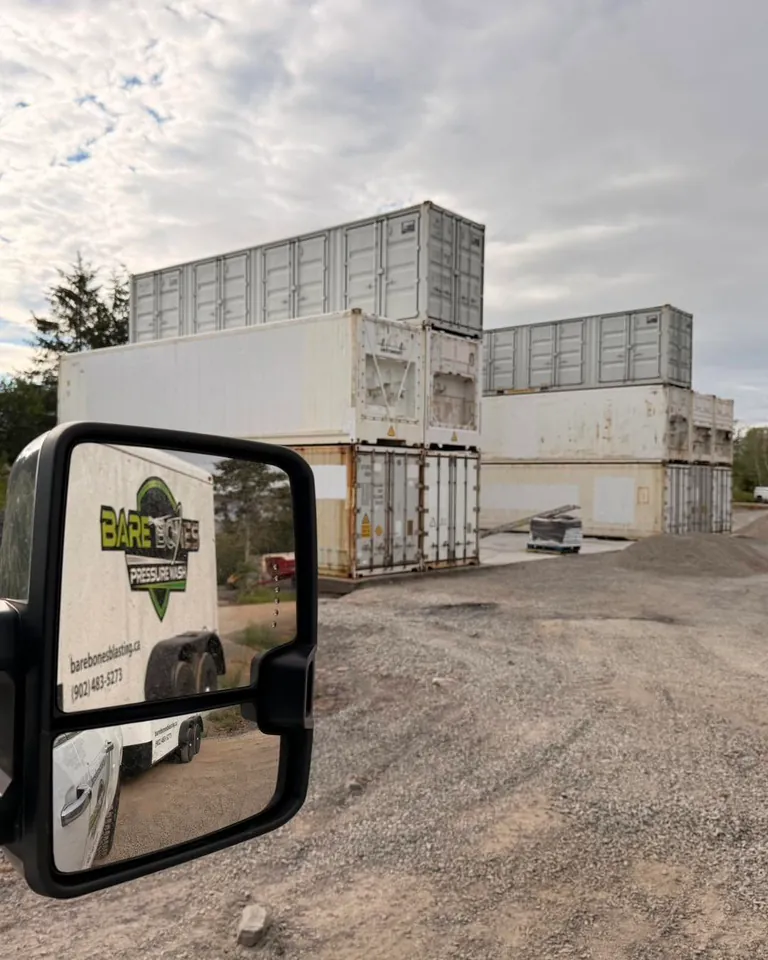 Bare Bones service trailer reflected in a truck mirror at a commercial sea-container site