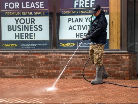 Peter pressure washing a brick sidewalk outside a downtown storefront