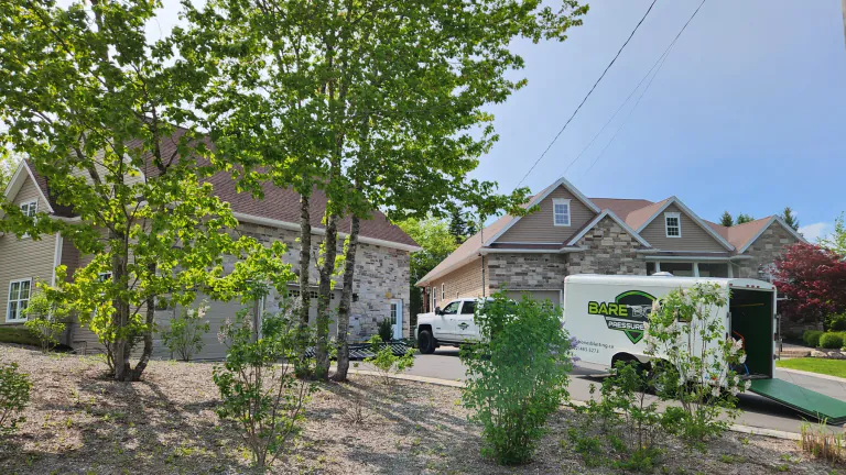 Bare Bones truck and trailer at a landscaped stone-front residential property on a sunny day