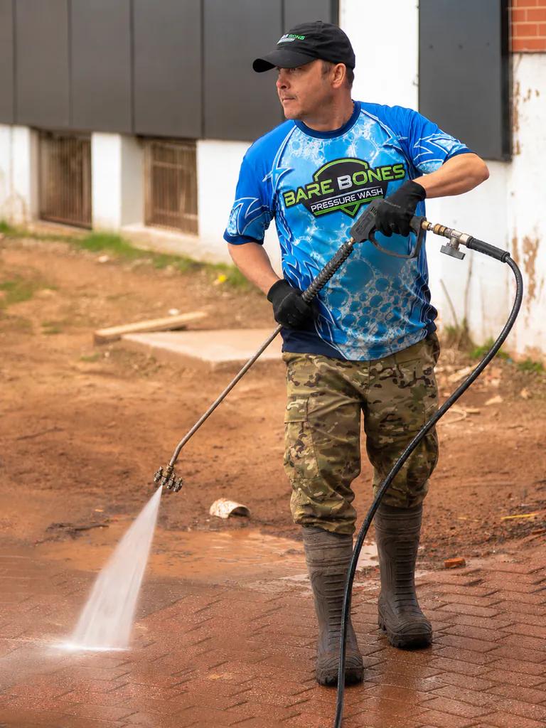 Peter, owner of Bare Bones Pressure Wash, pressure washing a brick surface in branded workwear