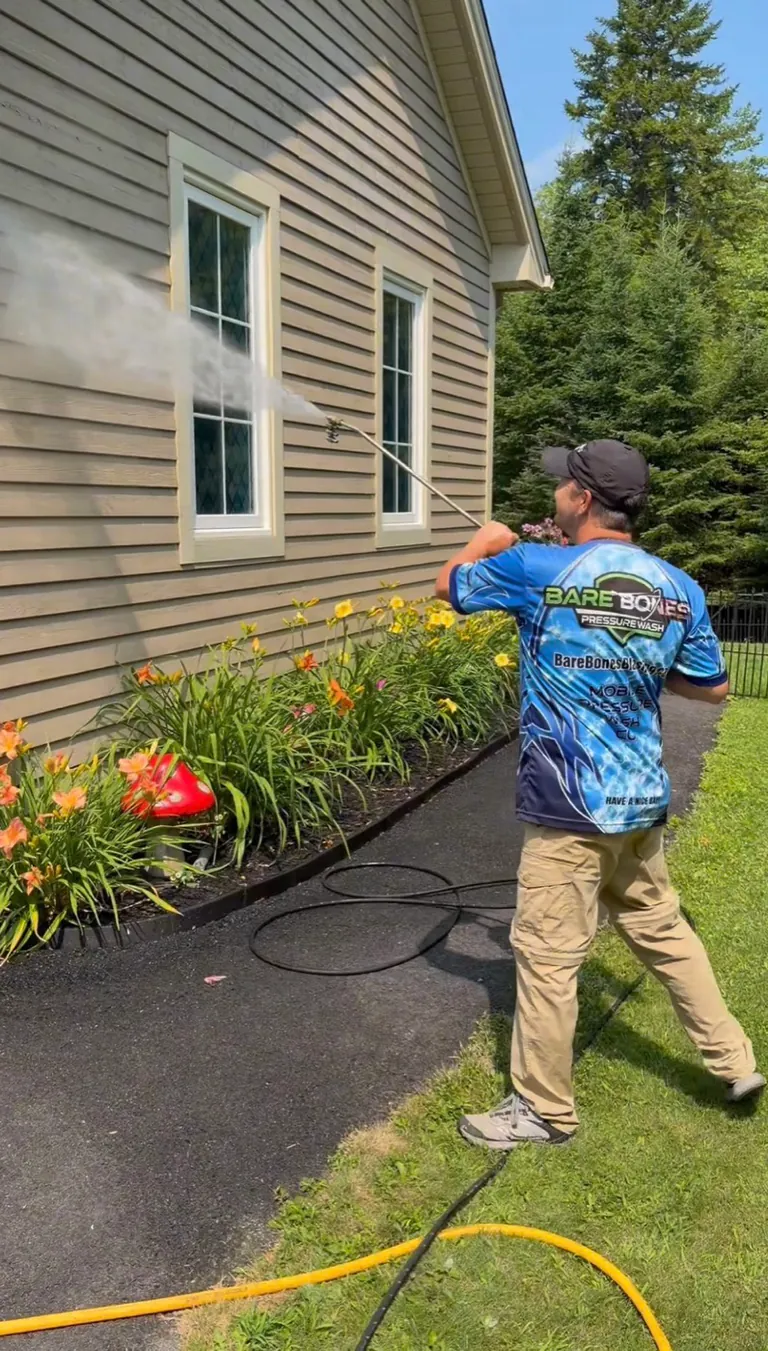 Peter soft washing home siding beside a carefully maintained flower garden