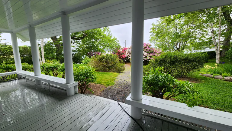 A freshly cleaned porch surrounded by mature shrubs, flowers, and garden beds